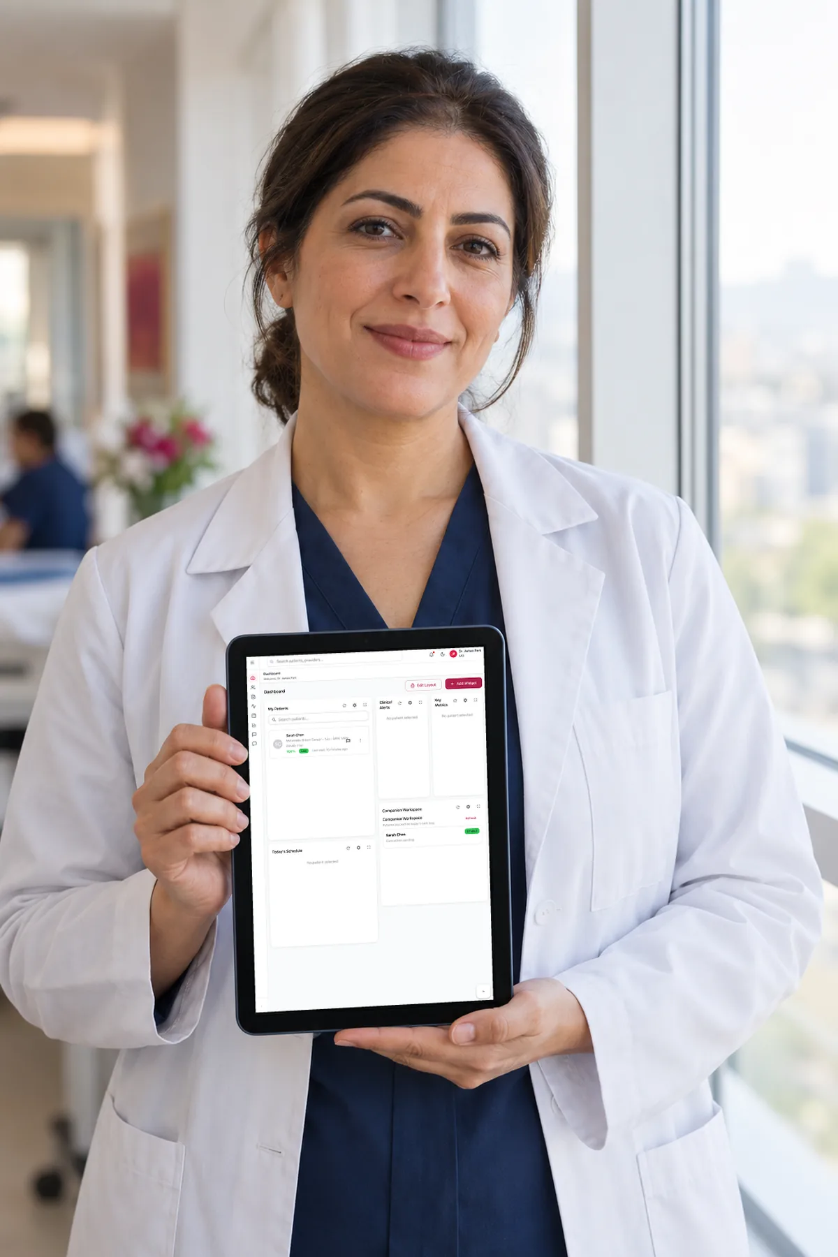 An oncologist in a white coat holds a tablet showing the MyBC clinician portal's patient overview and smiles at the camera.